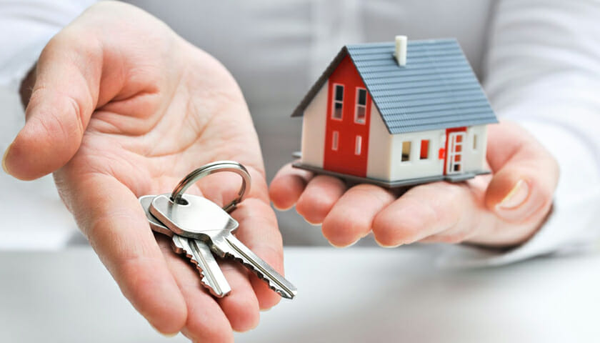 Close up of Mans hands with house keys in the left and a tiny house in the other