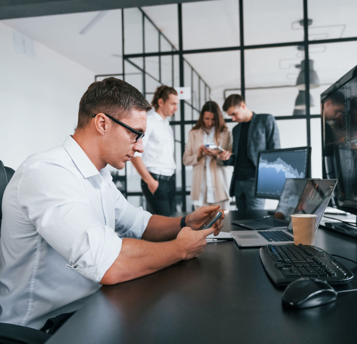 Get help with your bookkeeping today! Image of an office worker using a mobile phone with colleagues in the background, illustrating a page about a bookkeeping service.