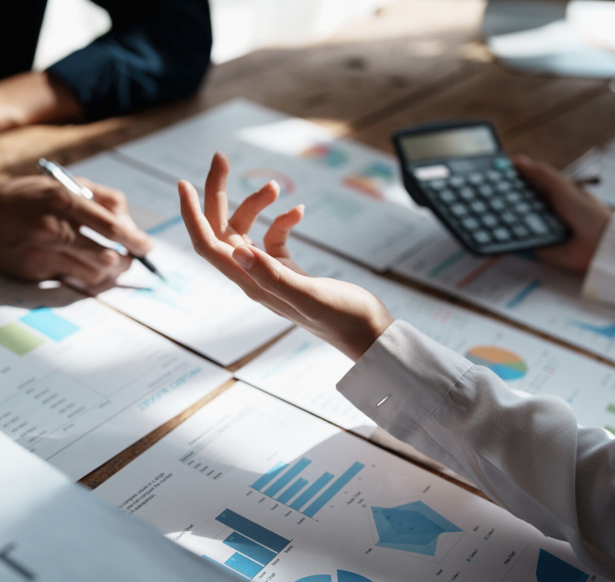 Closeup of two people's arms. One is writing and the other is holding a calculator. There are also lots of graphs on pieces of paper. This image illustrates a service page about Corporation Tax.