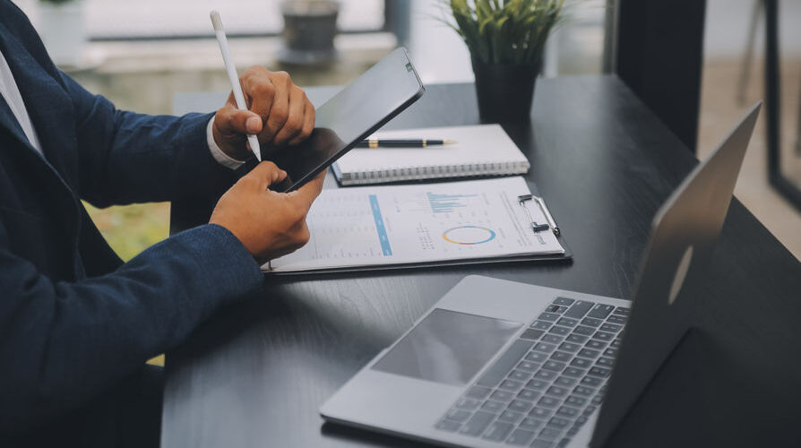 Image of a man working in an office with a tablet and laptop, illustrating a page about Corporation Tax services.
