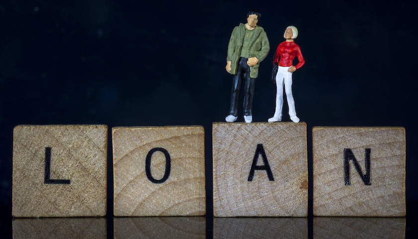 Two miniature model people standing on wooden blocks that spell the word 'LOAN'. This illustrates an article on overdrawn director's loan accounts.