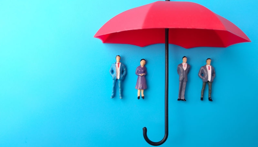 An image of miniature people standing under a red umbrella - to illustrate an article on umbrella company compliance.