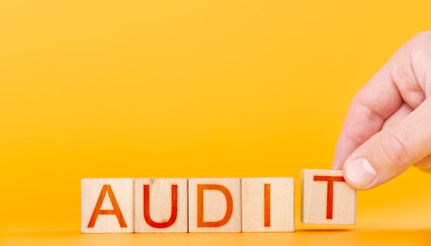 A hand puts wooden cubes into the word audit on orange background - to illustrate an article on voluntary audit