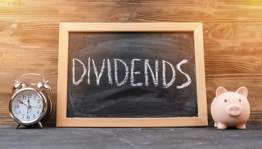 The word dividends on a black chalk board in a frame standing next to an alarm clock and a piggy bank - to illustrate an article on salary vs dividends 2026/27