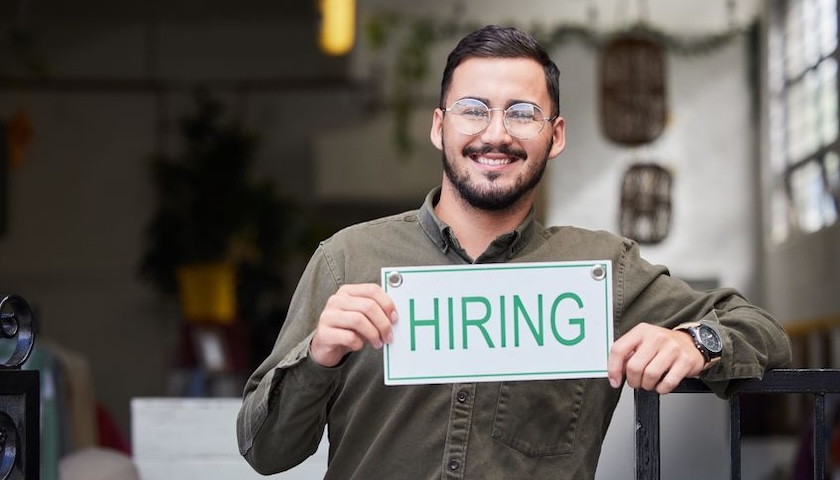 A man holding a sign with the word 'HIRING', illustrating an article on the true cost of hiring an employee UK