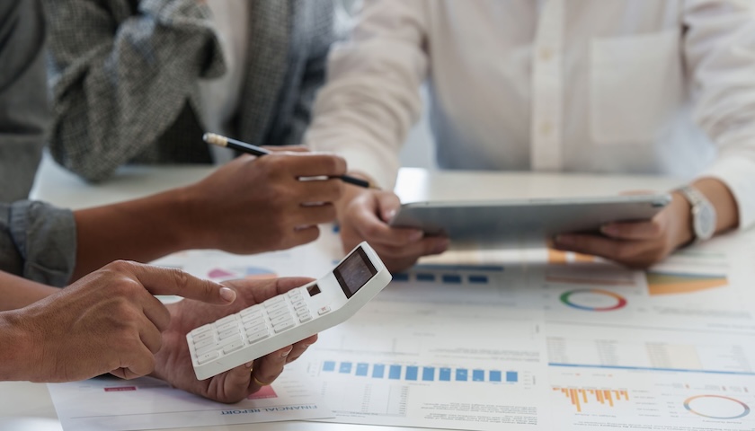 An image of three people's hands working on financial figures, illustrating a blog post that guides readers through a management accounts example.
