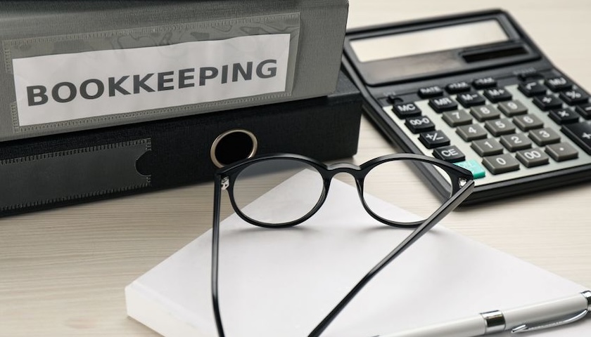 A bookkeeper's workplace with folders, glasses and stationery on wooden table, to illustrate an article about what a suspense account is.